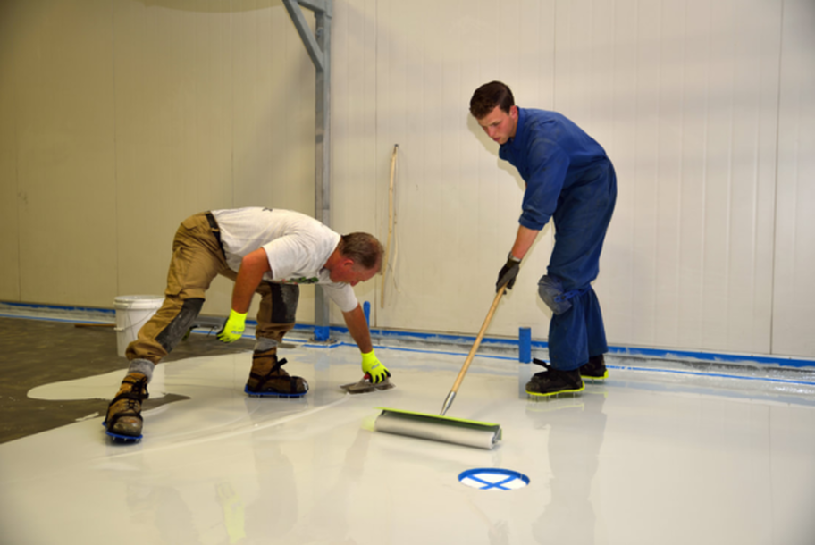 Two employees of Plancher Epoxy Magog apply the epoxy on the floor with a trowel and a roller.